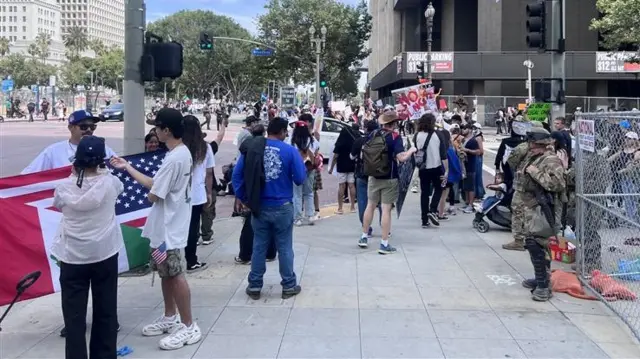 Protesters stand on a sidewalk as National Guard troops stand guard