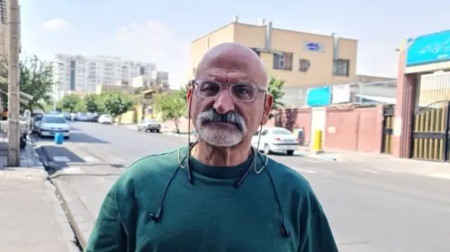 A bald man stands on a street in Tehran looking at the camera.