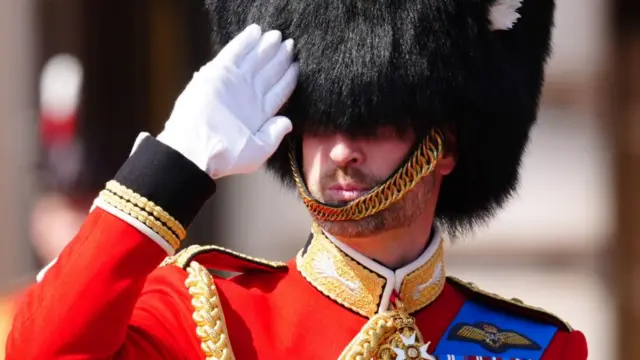 William wears Welsh Guards uniform, including a red jacket and black furry hat.