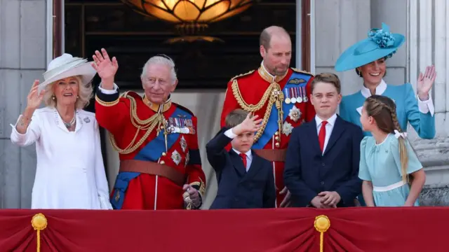 Charles, Camilla, William, Kate and their three children smile and wave on the palace balcony.