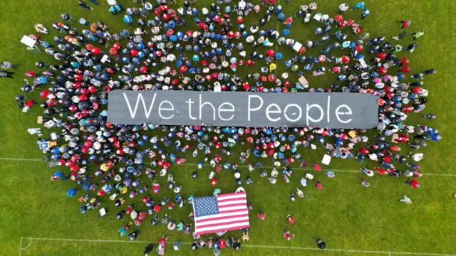 An aerial view of a group of people on a soccer field holding a huge sign that reads "We the people".