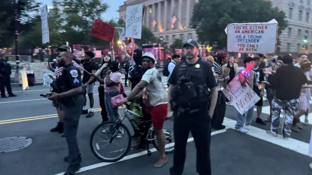 Two police officers stand in front of a group of protesters holding signs