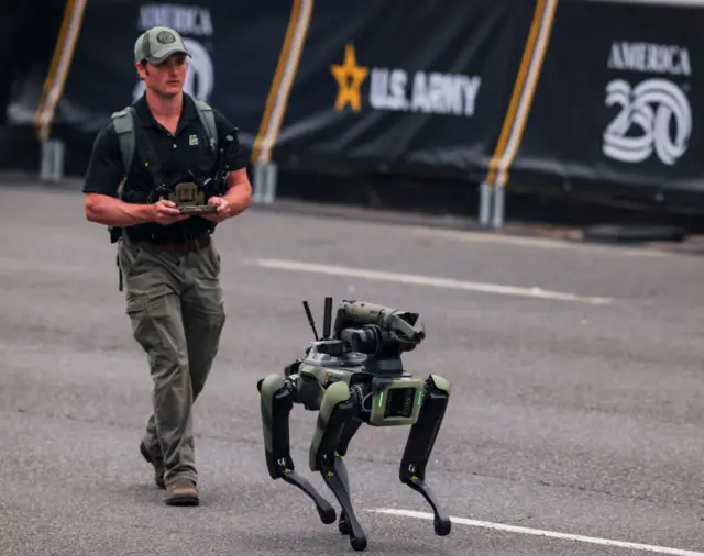 A person in tactical gear controls a quadrupedal robot during the U.S. Army's 250th Birthday parade