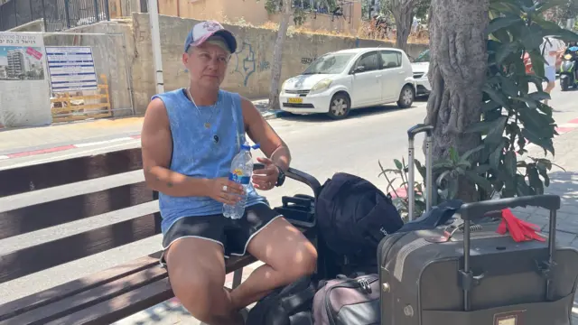 Katya sat on a bench, surrounded by bags and suitcases.