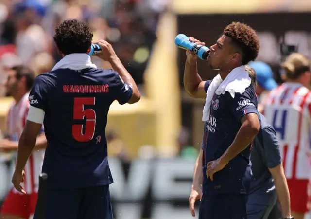 Doue and Marquinhos drink water during a break with wet towels draped around their shoulder