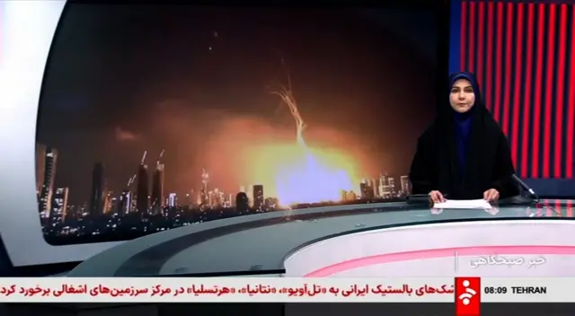 A news reader sits at a desk in front of an image of an exploding missile strike. below her is a news ticker written in arabic with the dateline 'tehran'.