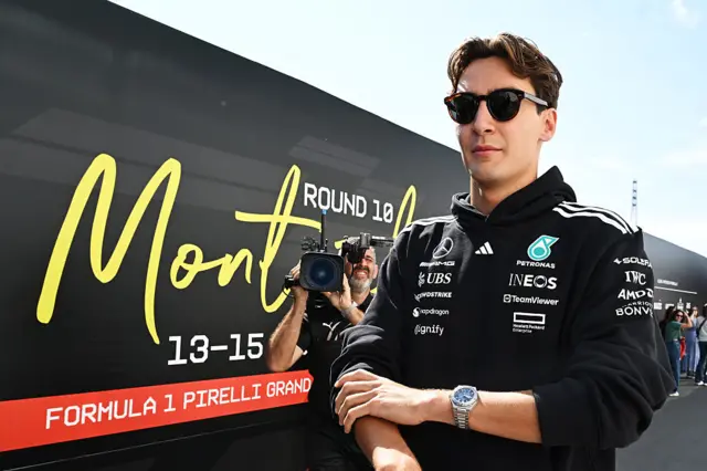 George Russell walks past a 'Montreal' sign in the paddock as a camera man films him