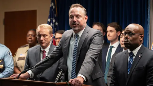 Acting U.S. Attorney Joseph H. Thompson speaking wearing a grey suit and blue tie