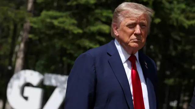 Donald Trump looks at the camera, with a G7 sign in the background and the sun shining on him