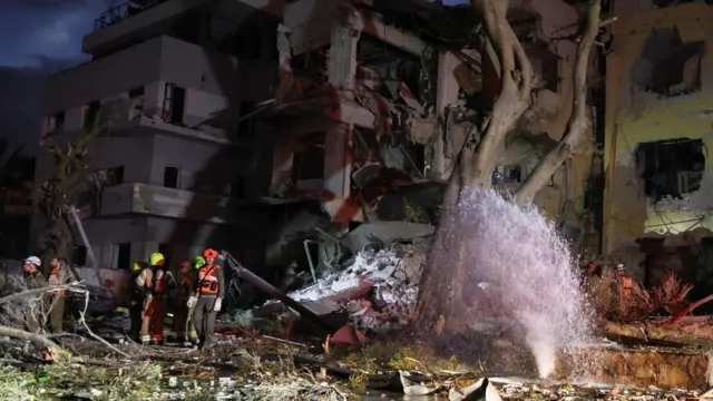 A heavily damaged building with rescue workers nearby