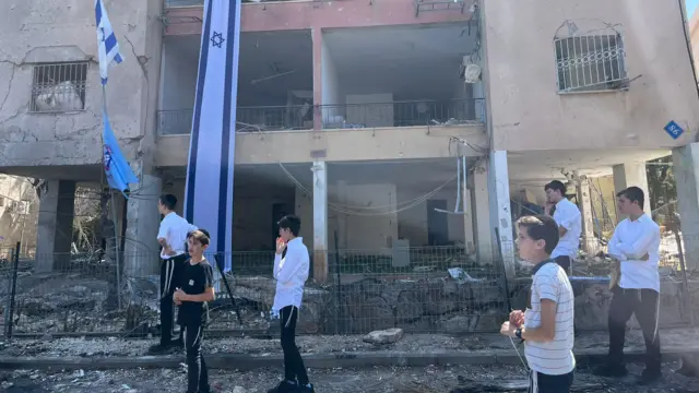 Children stand in the shadow of a building struck by Iranian strike in Haifa, Israel.