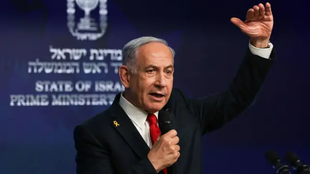 Benjamin Netanyahu raises his hand in gesture as he speaks into a microphone
