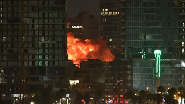 Orange flames and black smoke from an Iranian missile billow into the sky in an urban area of Tel Aviv.