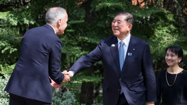Japan's Prime Minister Shigeru Ishiba and his wife Yoshiko smile and shake hands with Carney