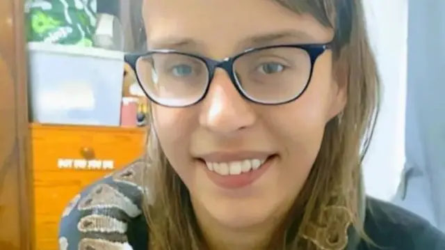 Teohna Grant smiles at the camera. She has short brown hair and wears glasses. There is a snake curled around her neck.
