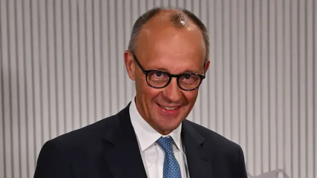 Merz close crop from shoulders up. he is smiling, wearing a blue patterned tie, white shirt and black blazer