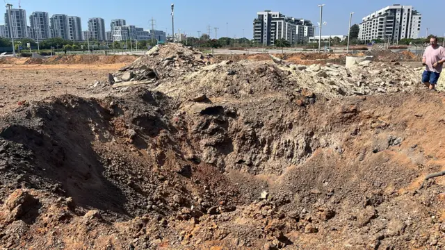 A large crater in the ground with buildings in the distance