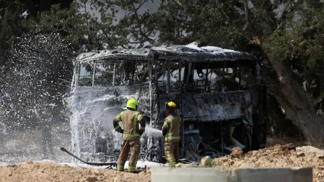 Firefighters spray water on a burnt-out bus