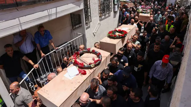 Dozens of people carry four wooden caskets down a narrow street