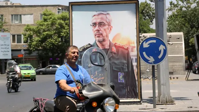 A large framed photo of Mohammed Bagheri on a busy street with a motorcyclist cycling past