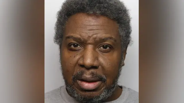 A custody image of Jazwell Brown. He is wearing a grey top and has short, greying hair and a grey beard.