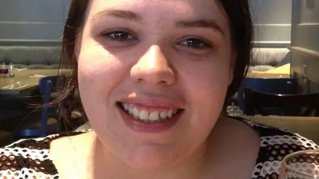 Joanne Pearson smiles at the camera. She has dark hair that is tied behind her head. She wears a white and brown striped top.