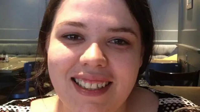 Joanne Pearson smiles at the camera. She has dark hair that is tied back and she wears a brown and white top.