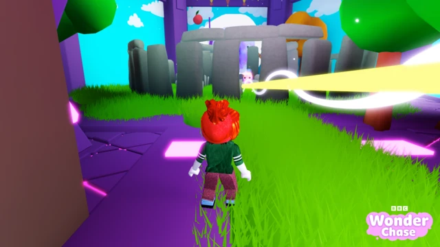 A computer game character with a red head, green top and purple trousers walks on bright green grass and purple ground. They are walking towards an animated version of Stonehenge.