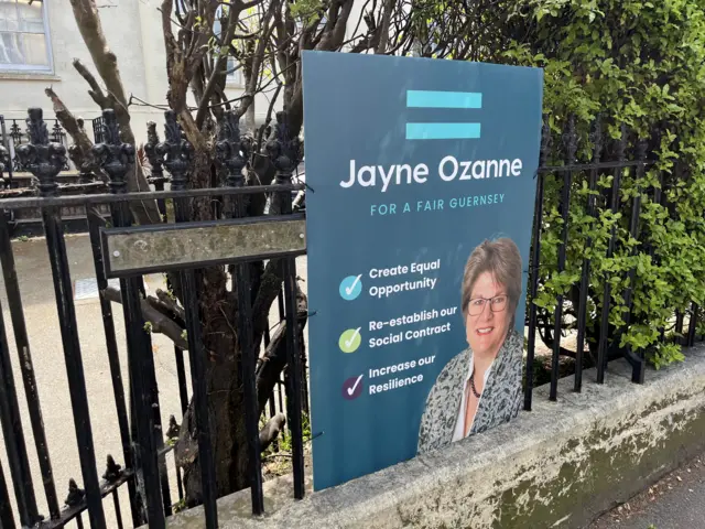 A large voting sign connected to a fence which says vote for Jayne Ozanne