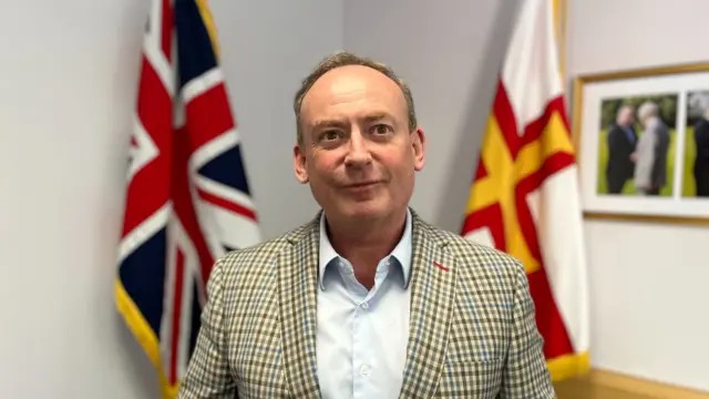 Lyndon Trott stood in a suit by flags