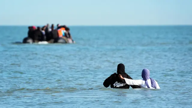 People thought to be migrants wade through the sea to board a small boat leaving the beach at Gravelines, Francein an attempt to reach the UK by crossing the English Channel.