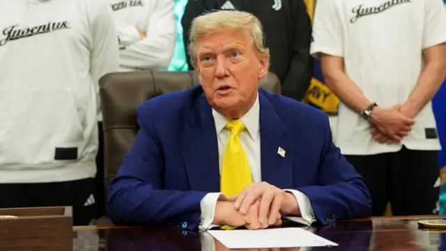 Trump at the desk in the Oval Office, wearing a yellow tie