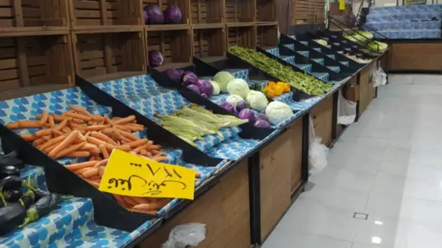 Some empty shelves interspersed with carrots and other vegetables in a shop