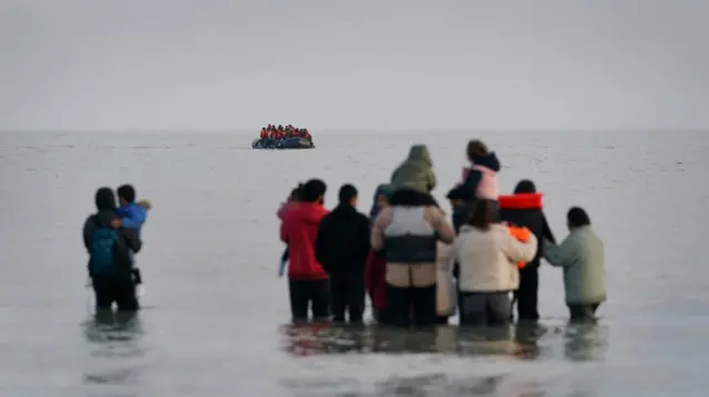 A group of people thought to be migrants wait in the sea to board an approaching small boat at Gravelines, France, in an attempt to reach the UK by crossing the English Channel.
