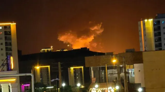 An image showing the blast in the Iranian capital. Smoke can be seen rising in the distance, with two high rise buildings in the foreground.