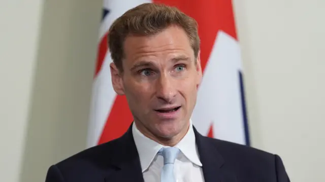 A file photo of Chris Philp - he is wearing a suit and sitting in front of a Union Jack flag