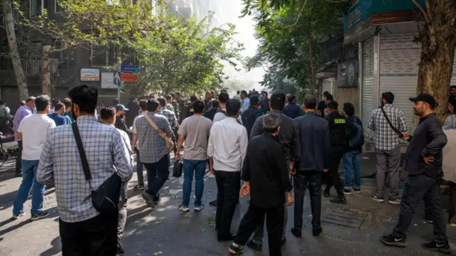 People gather in the street amid smoke following the Israeli strikes on Iran, in Tehran