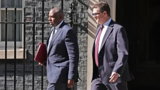 David Lammy walks beside another man, both in suits, outside the black railings of Downing Street