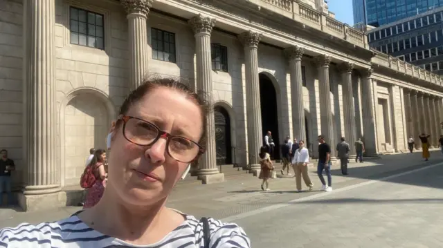 BBC business reporter Dearbail Jordan, wearing brown glasses and a white striped top, outside the Bank of England building in central London