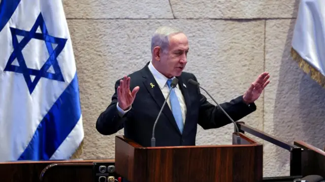 Israeli PM Benjamin Netanyahu stood behind podium with microphones, Israeli flag behind him.