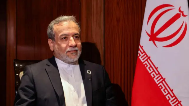 Iranian Foreign Minister Abbas Araghchi is pictures sitting next to a large Iranian flag.