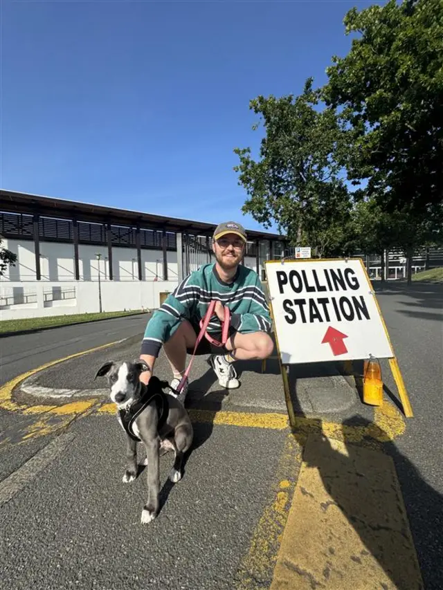 Tim Hunter crouched by a polling station sign with his dog