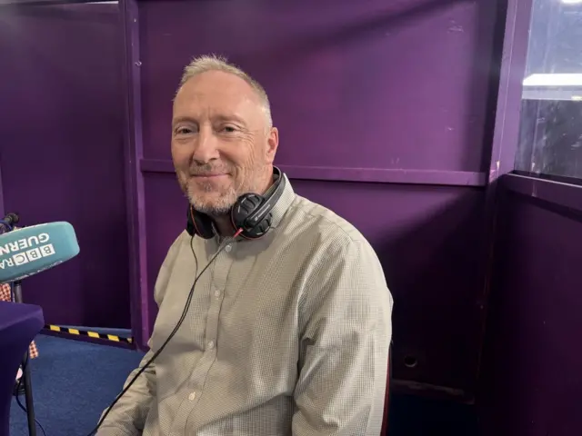 Man in pale shirt sitting in front of a microphone