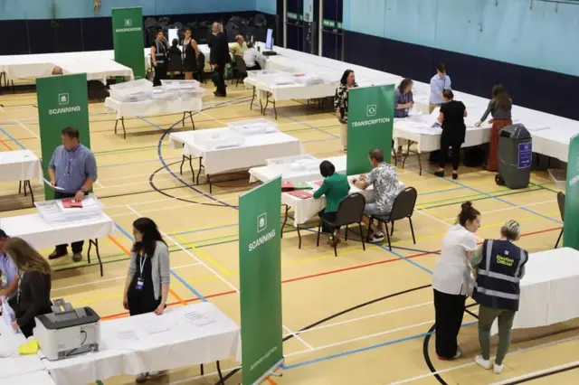 People stood and sat around voting tables in a sports hall