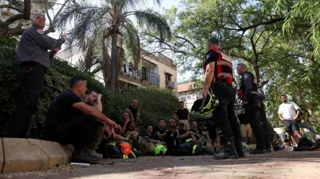 Emergency personnel gather at an impact site following a missile strike from Iran on Holon