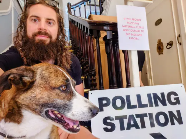 Leon Howard by a polling station a sign with his dog.
