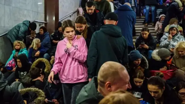A girl in a pink top stands in an underground station in Kharkiv while others sit around her