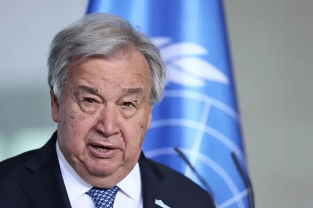 Guterres speaking in front of a UN flag