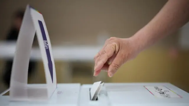 A close-up shot of a hand casting a ballot paper into a box.