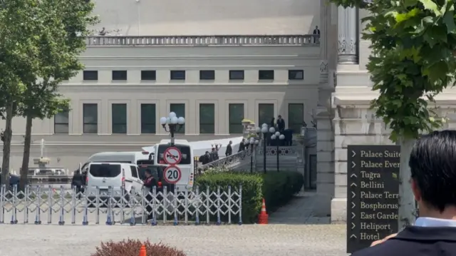 A photo taken outside the venue, coaches and vans can be seen as people walk up to the entrance